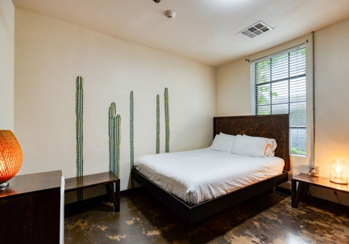 Queen bed with dark wood headboard, cactus wall decor, polished concrete floors