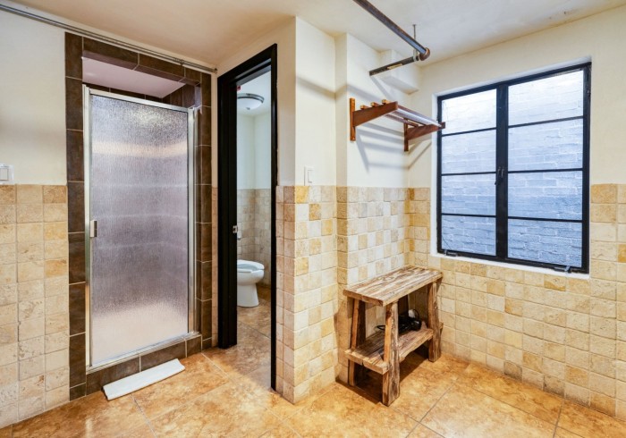 Private bathroom with travertine tile, glass shower door, and rustic wooden bench